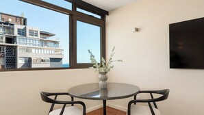Een moderne eetruimte met een ronde tafel, twee stoelen, een vaas met groen, een groot raam en uitzicht op een gebouw.