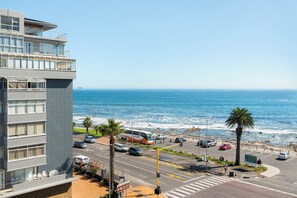 A coastal hotel with a view of the ocean, a parking lot, and a street with vehicles. - Seaside Stay | Prime Location and Views (Cape Town)