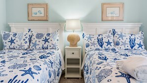 Ein Zimmer mit zwei Betten, beide mit Stichmotiven von Seesternen und Muscheln, einem Nachttisch mit Lampe und gerahmten Bildern an der Wand.