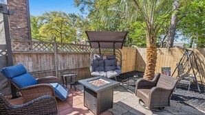 Eine Terrasse mit Korbmöbeln, einem Feuerkorb und einem Holzzaun.