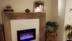 A living room with a fireplace, a flat-screen TV, and potted plants.