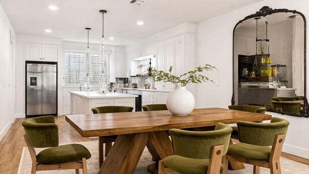 A modern kitchen with white cabinets, a wooden dining table, and green chairs.