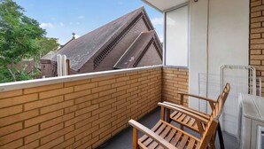 Een balkon met een bakstenen muur, een houten stoel en een metalen hekwerk.