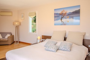 Ein Schlafzimmer mit einem Bett, einem Nachttisch mit Lampe, einem Fenster und einem Bild an der Wand.