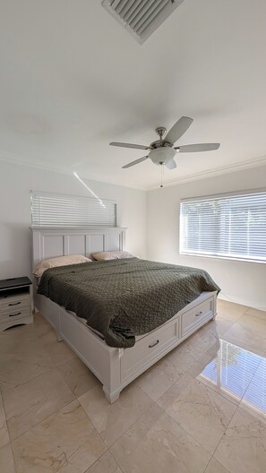 A bedroom with a bed, a ceiling fan, a window with blinds, and a nightstand. - Coral Gables Vacation House with Pool (Coral Gables)