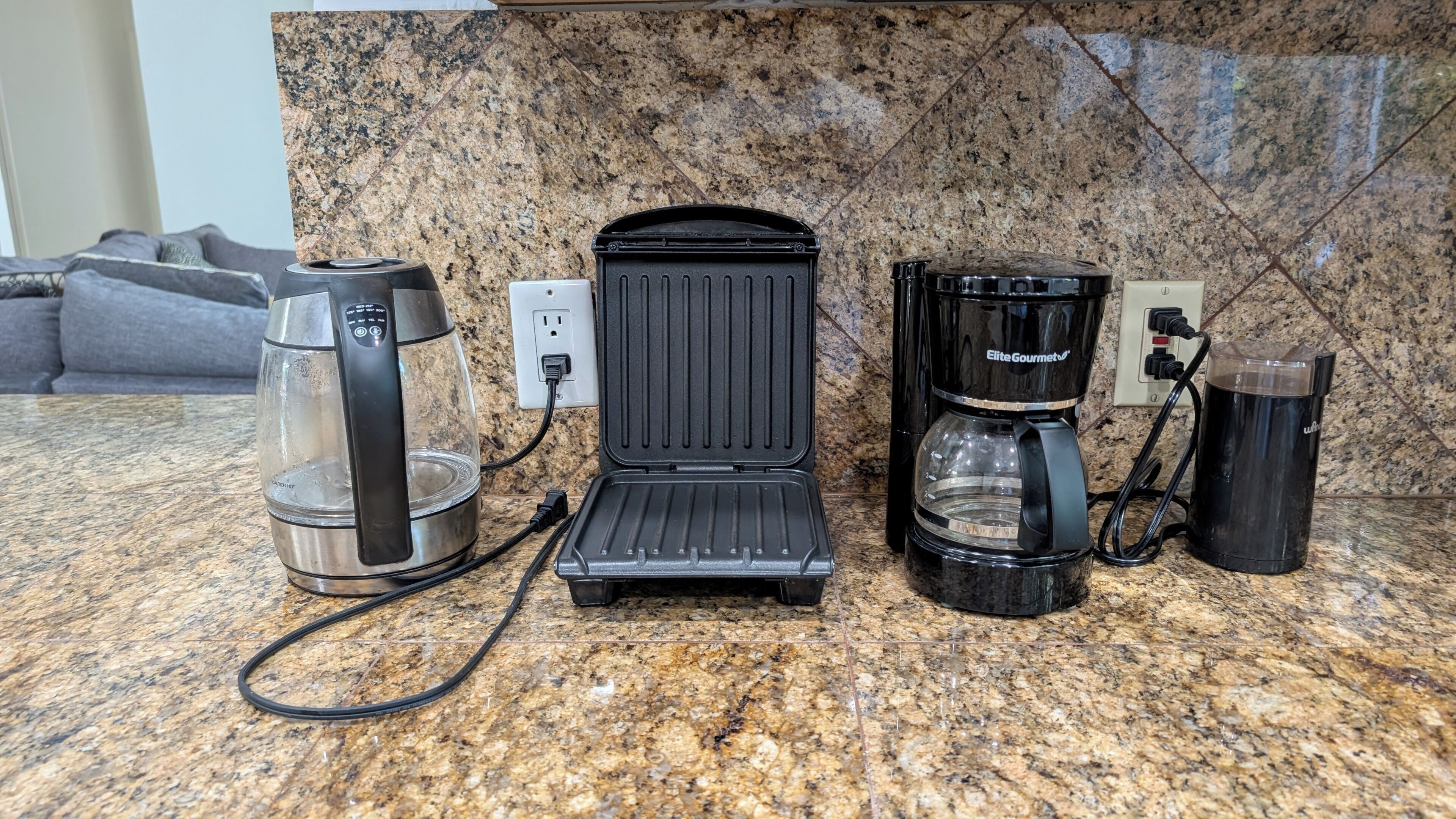 Una cocina con cafetera, plancha para gofres y una taza sobre una encimera de granito.