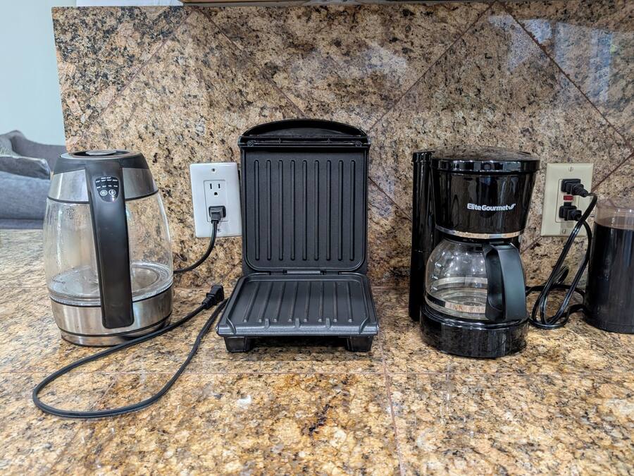 Una cocina con cafetera, plancha para gofres y una taza sobre una encimera de granito.