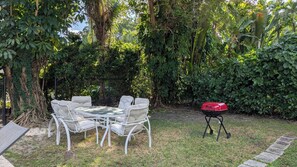 An outdoor seating area with a table and chairs, surrounded by dense foliage and a barbecue grill. - Coral Gables Vacation House with Pool (Coral Gables)