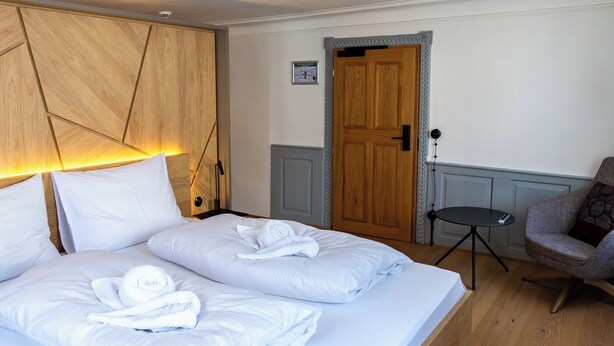 A hotel room with a wooden bed, a desk, and a chair. - Münsterhus Josefs Alpine Lodge - Three Towers Triple Room (Schruns)
