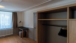 A room with a wooden floor, a desk with a chair, a radiator, a wardrobe with hanging space, and a window with curtains. - Münsterhus Josefs Alpine Lodge - Three Towers Triple Room (Schruns)
