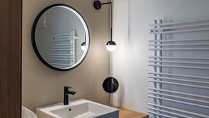 A modern bathroom with a white sink, a round mirror, and a wall-mounted heater. - Münsterhus Josefs Alpine Lodge - Three Towers Triple Room (Schruns)