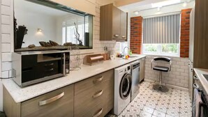 A compact kitchen with a microwave, washing machine, and a bar stool. - Beautiful Escape | Wi-Fi | Garden & Free Parking - Pass the Keys (Nottingham)