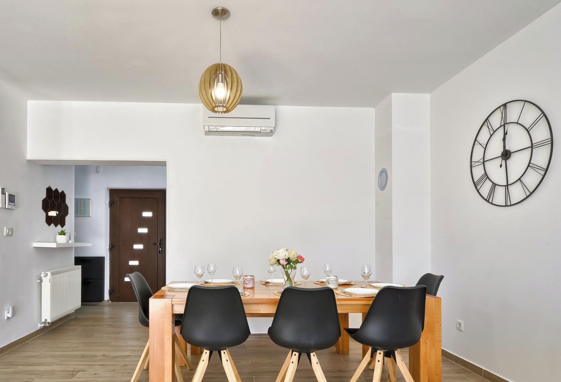 Un coin repas avec une table en bois, des chaises noires, une horloge murale et une suspension.