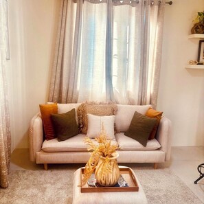 A living room with a sofa, decorative pillows, a vase with dried plants, and a tray with a book.