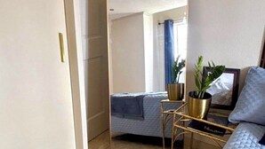 A room with a bed, a mirror, a bedside table with a plant, and a window with curtains. - Cazuria - by Zenbreak (Newbury)