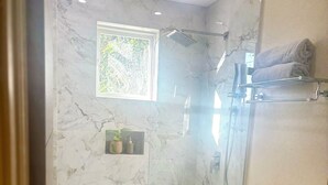 A bathroom with a shower, toilet, and a small shelf with a plant. - Cazuria - by Zenbreak (Newbury)