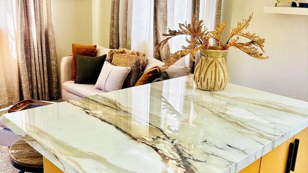 A kitchen with a marble countertop, a yellow cabinet, and a vase with dried plants. - Cazuria - by Zenbreak (Newbury)