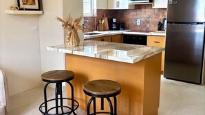 A modern kitchen with a central island, bar stools, pendant lights, and stainless steel appliances. - Cazuria - by Zenbreak (Newbury)