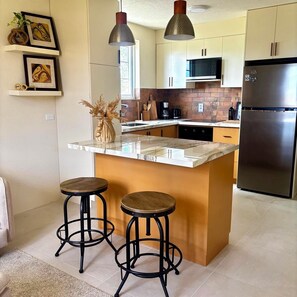 A modern kitchen with a central island, bar stools, pendant lights, and stainless steel appliances. - Cazuria - by Zenbreak (Newbury)