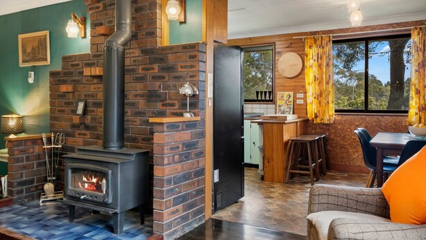 Un cuarto acogedor con chimenea de ladrillo, una zona de comedor con mesa y sillas de madera, y vistas a través de una ventana con cortinas.