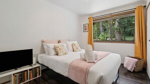 Un dormitorio con cama, televisión, estantería y ventana con cortinas.