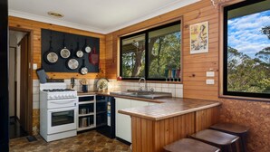 Una cocina con estufa a gas, horno, pileta y ventana con vista a árboles.