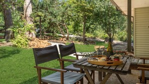 Un patio al aire libre con una mesa de madera, dos sillas y una botella de vino.