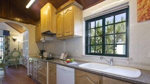Une cuisine avec des meubles en bois, un lave-vaisselle encastré, une grande fenêtre donnant sur un espace verdoyant et un plan de travail sur lequel sont disposés divers ustensiles de cuisine.
