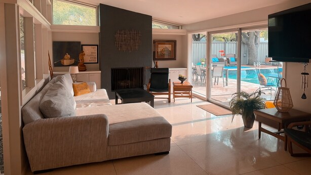 Una sala de estar moderna con chimenea, un sofá, un televisor y vista a una piscina.