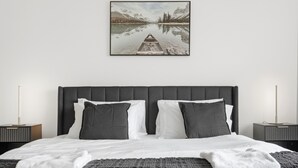 Quarto moderno com uma cama grande, cabeceira, duas mesas de cabeceira e um quadro emoldurado na parede.