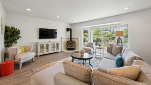 Una sala de estar con chimenea, sofá, televisor y ventanas amplias.