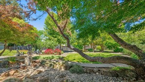 Un jardín con un sendero de piedra, un banco de madera y diversas plantas y árboles.