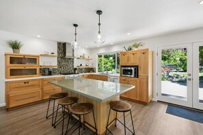 Eine moderne Küche mit einer großen Kochinsel, Holzschränken und Pendelleuchten.
