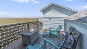 Eine Terrasse mit Feuerstelle, Gartenmöbeln und Blick auf den Strand.
