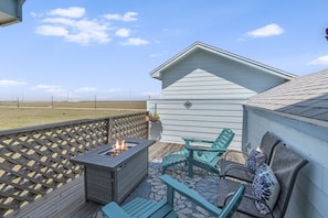 A deck with a fire pit, outdoor furniture, and a view of the beach.