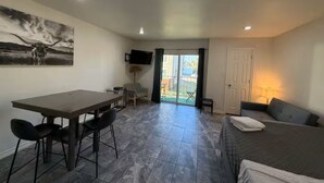 A room with a bed, a desk with chairs, a TV, and a sliding glass door to the outside. - 1-bedroom studio with AC in vibrant TX (Austin)