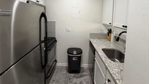 A compact kitchen with a stainless steel refrigerator, a trash bin, a sink, and white cabinets. - 1-bedroom studio with AC in vibrant TX (Austin)