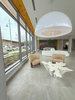 A spacious lobby with large windows, a modern ceiling light, and a unique white coffee table.