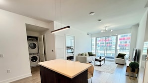 Un appartement moderne doté d’un îlot central, d’un lave-linge, d’un canapé, d’une table basse et d’une grande fenêtre offrant une vue sur la ville.