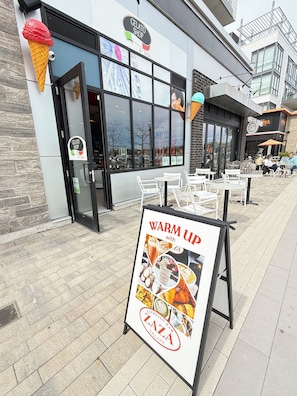 A storefront with a sign for 'Gelato Shop by Zaza' and a 'Warm Up with LAZA' advertisement.