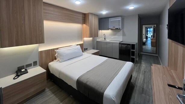 A modern hotel room with a bed, bedside table, and a small kitchenette. - Modern loft City Bog Usaquén (Bogotá)
