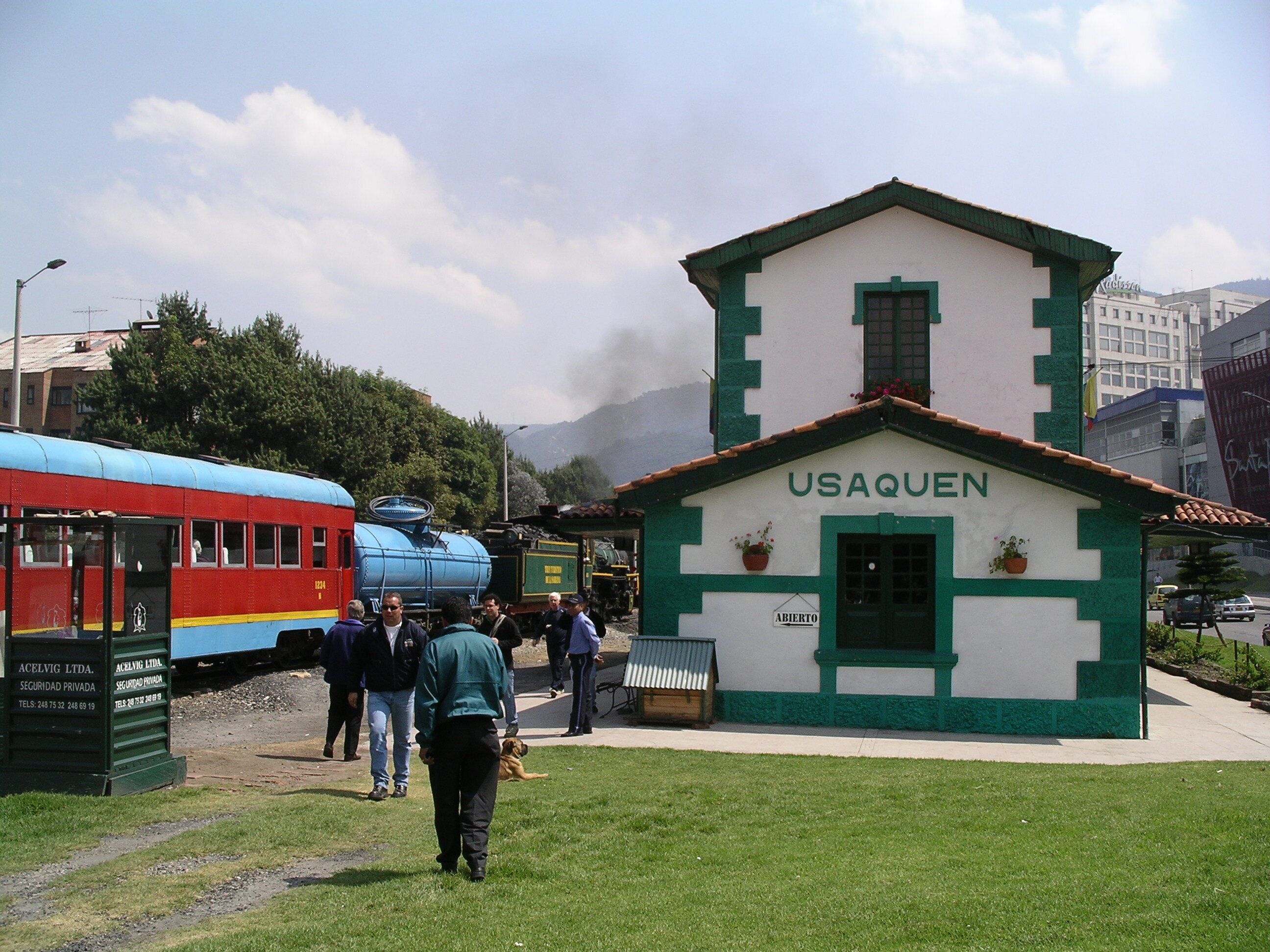 A building labeled 'USAQUEN' with a green and white facade, a small porch, and a sign indicating 'ABIERTO' (open).