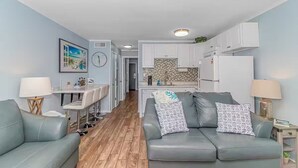 Ein modernes Wohnzimmer mit grauem Sofa, einem Essbereich mit weißem Tisch und einer Küche mit weißen Schränken und einer gefliesten Spritzschutzwand.