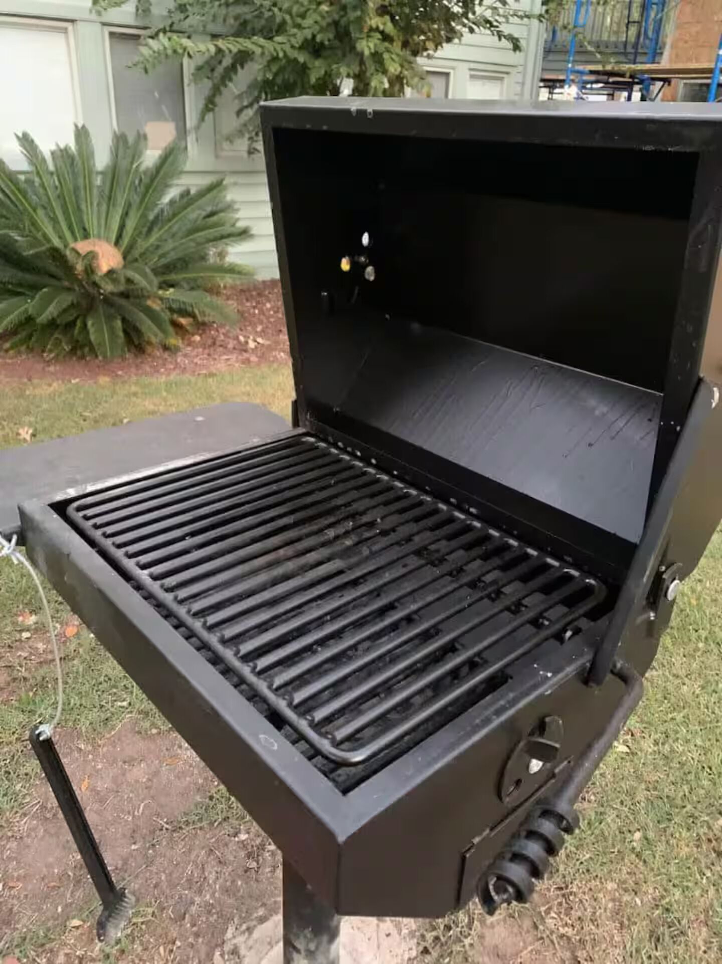 Un barbecue noir doté d’une grille inclinée, d’un panneau de commande et d’un tuyau à gaz.