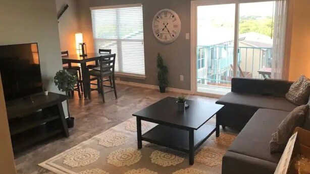 Una sala de estar con sofá, una mesa de centro, televisor, mesa de comedor y sillas, y un ventanal grande.