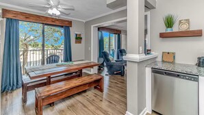 Eine moderne Küche mit Geschirrspüler, ein Essbereich mit Holztisch und Bank sowie ein Balkon mit blauen Vorhängen.