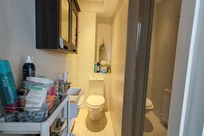 A compact bathroom with a toilet, a shelf with toiletries, and a small mirror. - Spacious Apartment Sleeps 7 Near Central London (London)