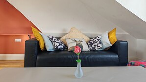 Ein Wohnzimmer mit einer schwarzen Ledersofa, einer weißen Vase mit einer einzelnen Rose und gemusterten Kissen.