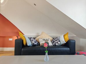 A living room with a black leather sofa, a white vase with a single rose, and patterned cushions. - Spacious Apartment Sleeps 7 Near Central London (London)