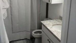 A compact bathroom with a shower curtain, toilet, and a marble countertop sink. - 1-bedroom studio in TX with AC for your stay (Austin)
